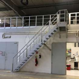 Escalera de acceso para entresuelo industrial con barandas añadidas para protección anti-caídas.